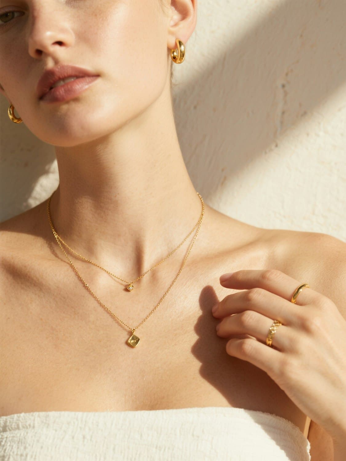 Close-up of layered gold necklaces, hoop earrings and rings worn in warm light
