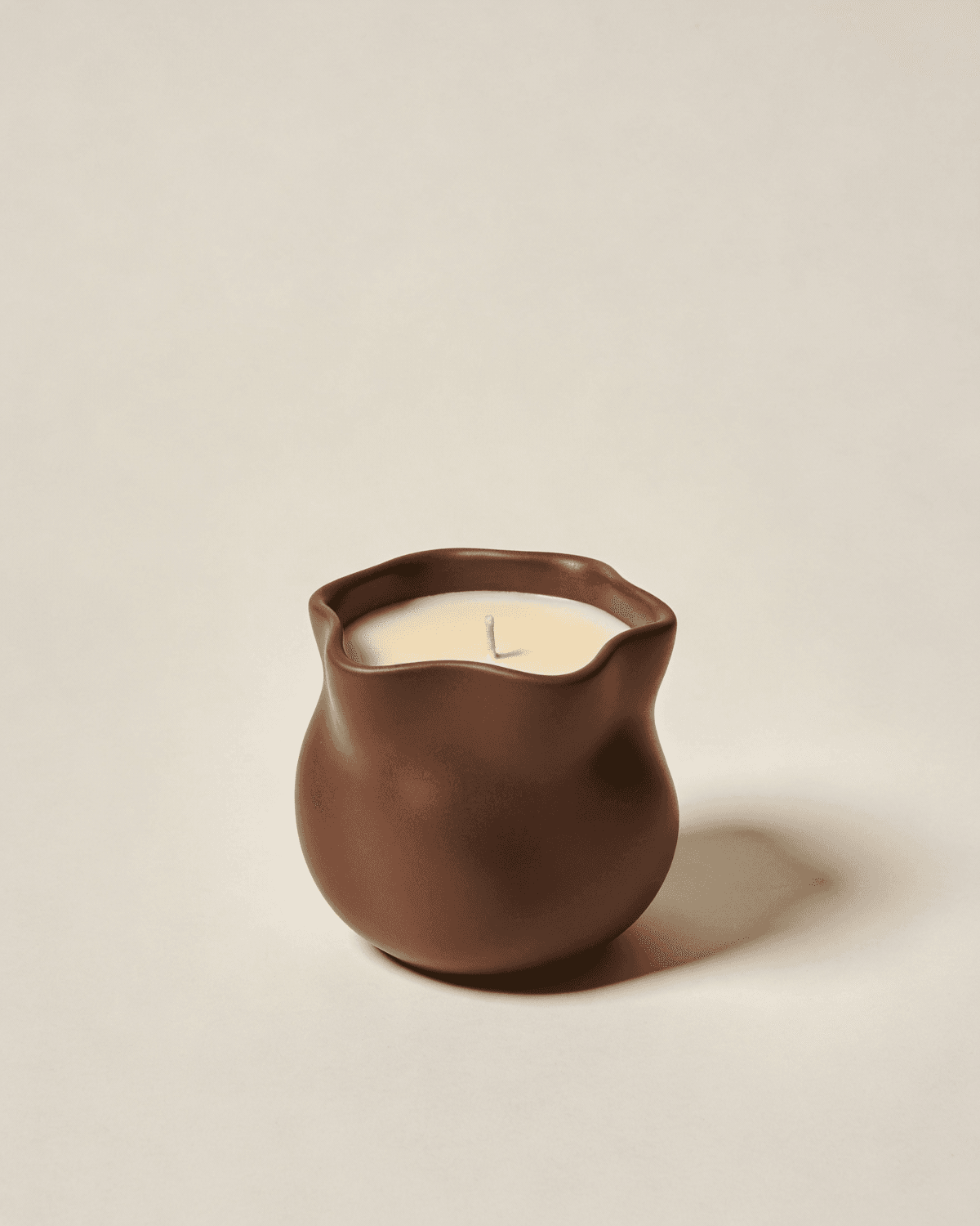 Scented candle in a sculpted brown stoneware vessel