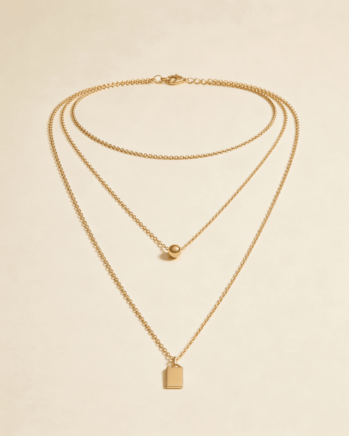 Three-strand gold necklace with a bead and a rectangular tag pendant