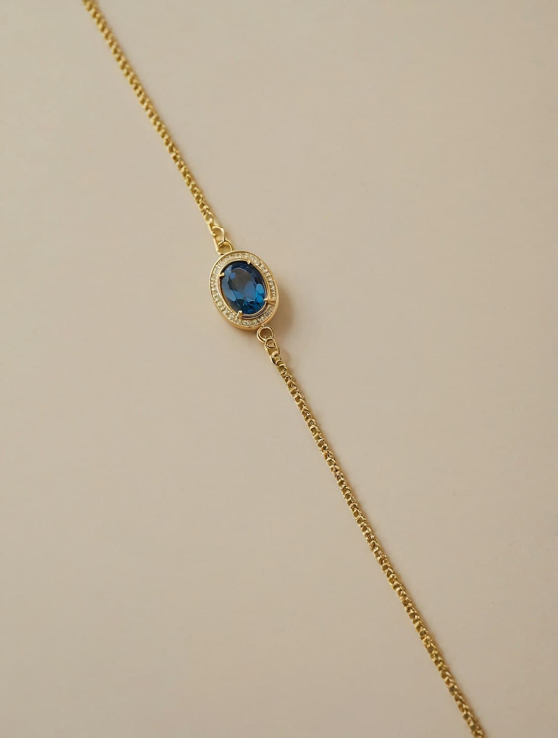 Gold chain bracelet with an oval blue sapphire in a diamond halo