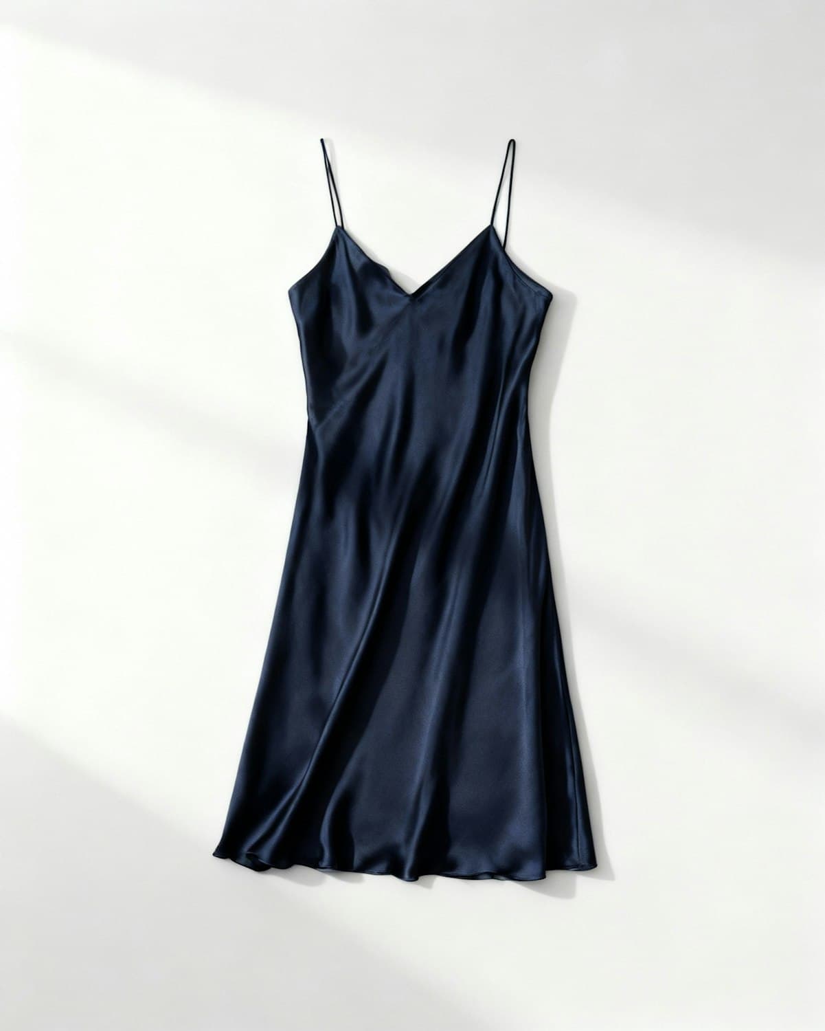 Midnight navy silk satin slip dress laid flat in soft window light