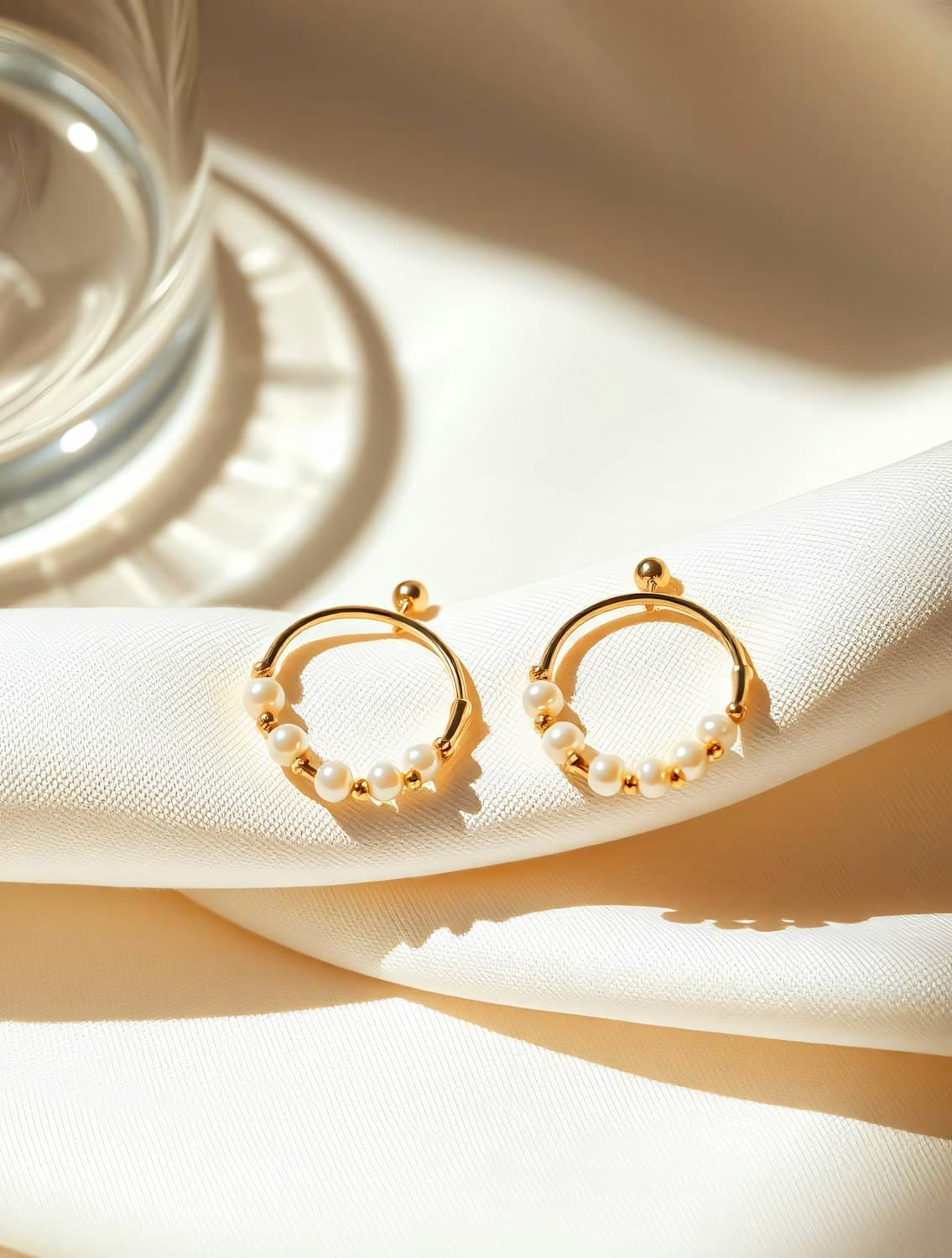 Pair of gold hoop earrings threaded with small pearls on cream silk